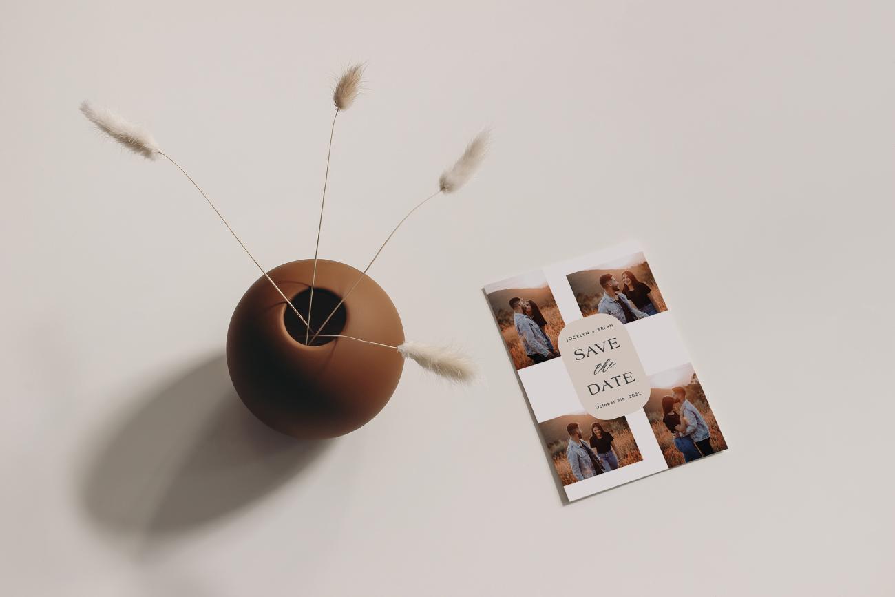 Save the date laying next to vase with twigs in it