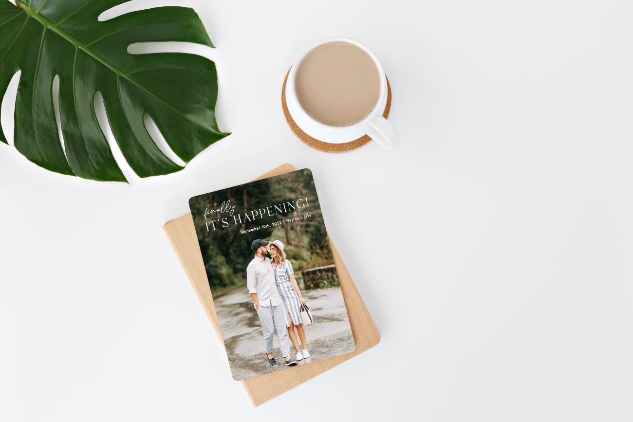 Save the date magnet laying next to leaf and cup of coffee