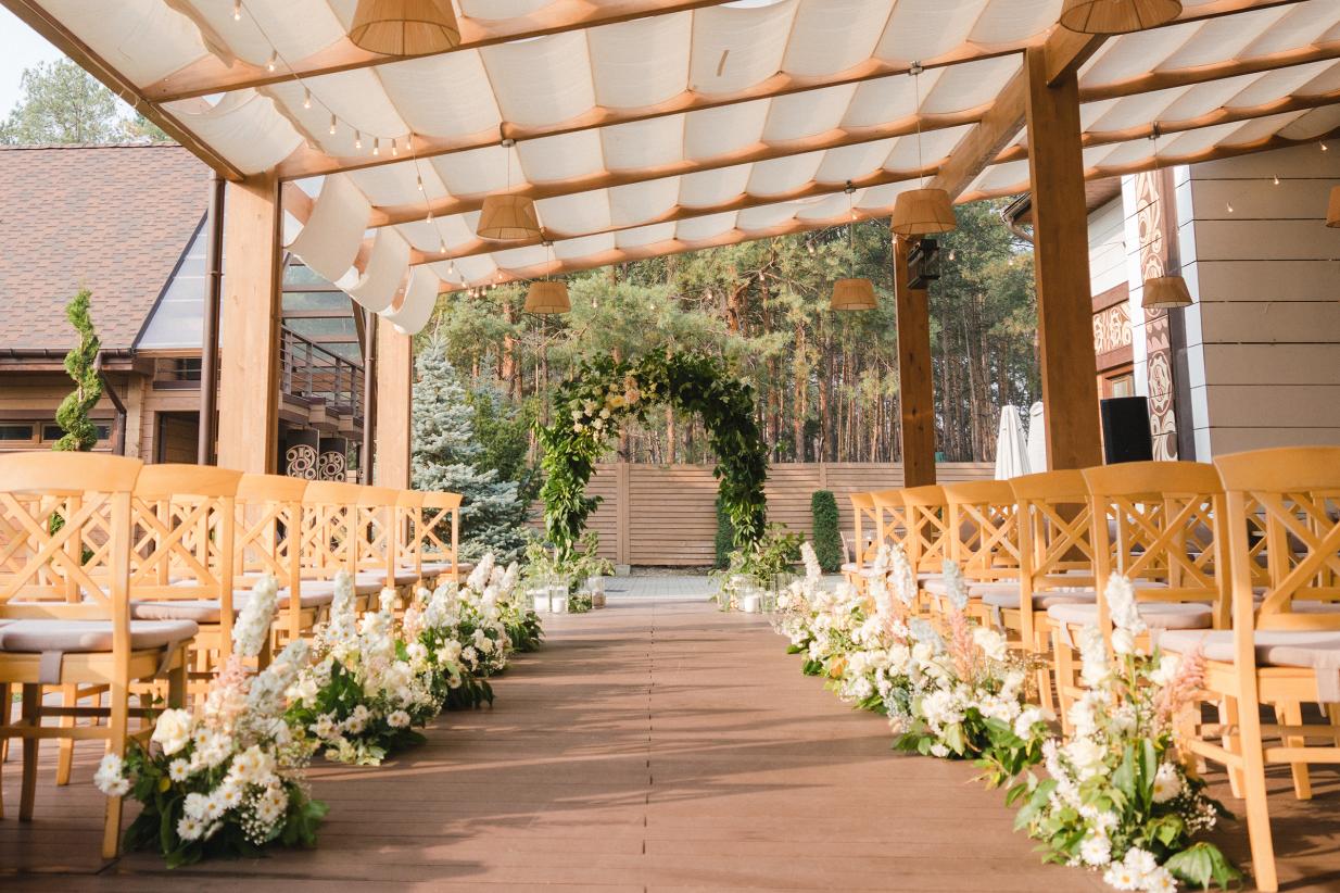 Beautiful wedding ceremony venue with wooden chairs and a green arch.
