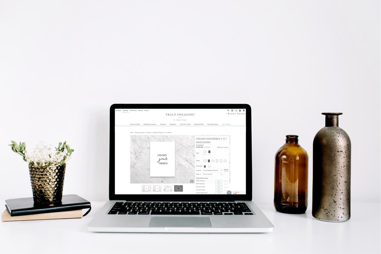 Laptop computer sitting on desk next to vases with upload your own design on the screen.