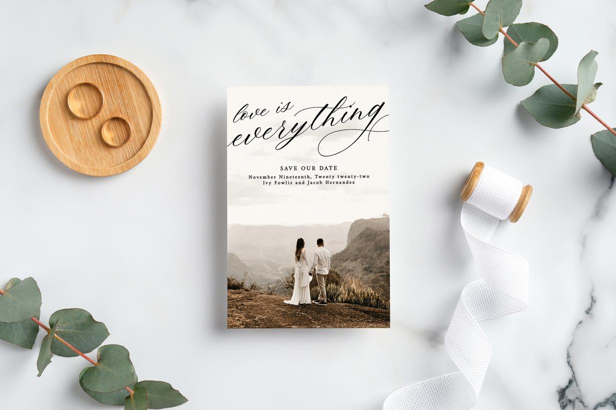 Photo save the date card on marble background next to rings and ribbon