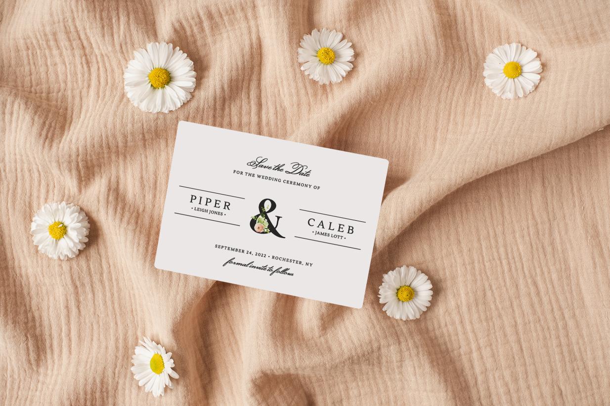 Save the date magnet laying on pink cloth surrounded by daisies