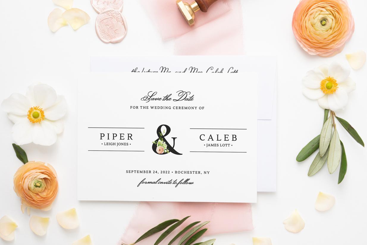 Save the date card on top of envelope surrounded by beautiful flowers, pink ribbon, and wax seals.